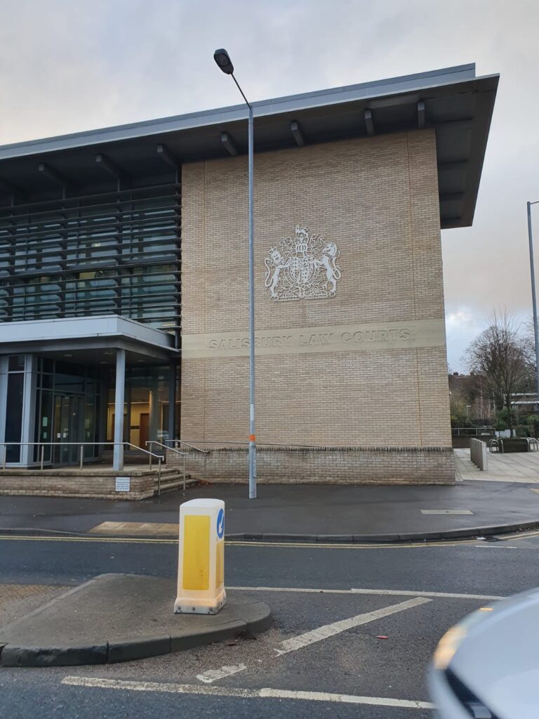 Modern building with large windows and brick facade displaying the words Salisbury Law Courts and a crest above the entrance, viewed from across the street.